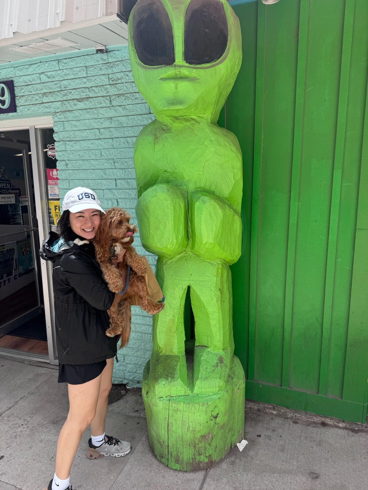 Molly holding Harold next to a green alien figure in Midtown Ruidoso